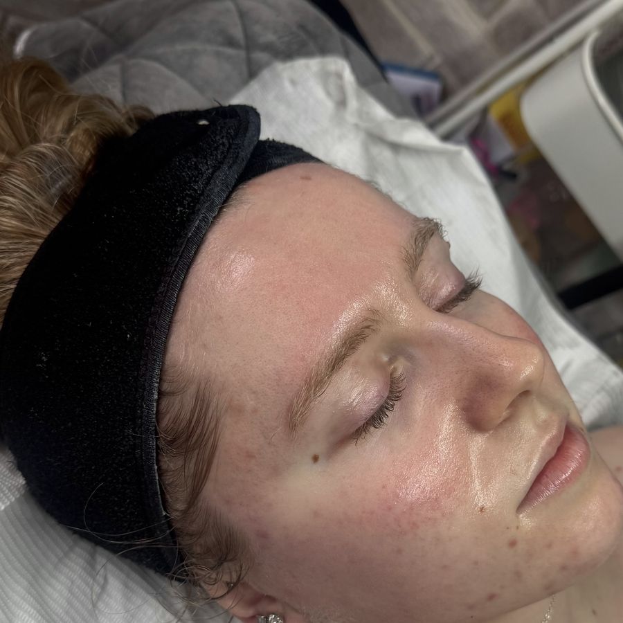 A client mid-facial treatment — glowing, freshly cleansed skin, wearing a spa headband in the studio.